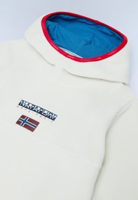 Pullover in pile crema con cappuccio blu bordato di rosso, caratterizzato da una toppa con logo e bandiera norvegese. Texture morbida, design moderno e alto collo.
