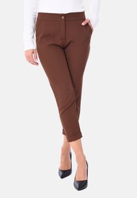 Pantaloni marroni a sigaretta con chiusura a bottone e passanti per cintura, dotati di tasche laterali e orli arrotolati, abbinati a tacchi neri a punta.