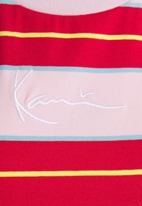 Sarkans un rozā svītrots audums ar zilo un dzelteno akcentu; rotāts ar izšūtu logotipu "Kani" baltā krāsā. Mīksts, teksturēts materiāls.