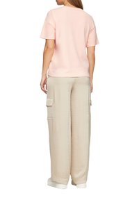 Jasnoróżowa bluzka z krótkim rękawem o prostym kroju, w zestawieniu z luźnymi beżowymi spodniami cargo z bocznymi kieszeniami o miękkiej teksturze.