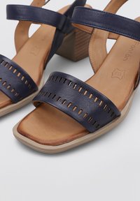 Sandalias de cuero azul marino con punta abierta, correas perforadas y una plantilla contorneada en tono bronceado. Tacón grueso estilo madera, suela de goma.