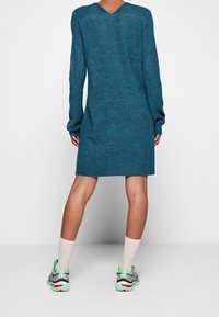 Abito lavorato a maglia in verde acqua con maniche lunghe, schiena a V e orlo a coste. Abbinato a sneakers con dettagli verdi e calzini rosa.