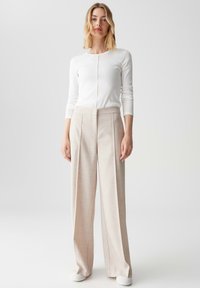 Witte lange mouwen ribbel top gecombineerd met wijde beige broek; de broek heeft een getextureerde stof en een op maat gemaakte uitstraling.