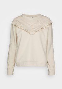Kremowa bluza z dekoltem w kształcie litery V wykończonym koronką i falbanami, z długimi rękawami i luźnym krojem. Miękka faktura materiału.