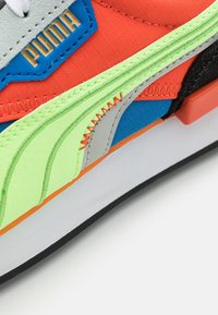 Teniska Puma s výraznou oranžovou, modrou a zelenou tkaninou. Má vrstvené textury, kontrastní prošití a výrazné logo.