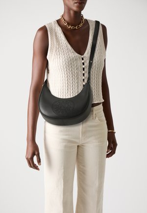 Black leather shoulder bag with a curved shape and perforated design on the front. Paired with a cream knit top and light-colored trousers.