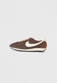 Brūni skriešanas apavi ar teksturētu auduma augšdaļu, baltu swoosh logotipu, krēmkrāsas akcentiem un melnu gumijas zoli ar saķeri.