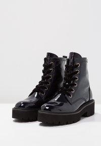 Bottines en cuir verni noir avec finition texturée, présentant un bout arrondi, un laçage à l'avant et une semelle épaisse en caoutchouc noir.