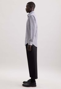 Langsleeve geruite shirt in wit en marineblauw, gecombineerd met zwarte op maat gemaakte broek. Het model draagt zwarte leren schoenen en sokken.