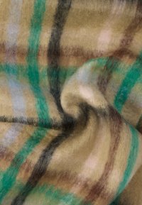 Mykt ullstoff med en lodden tekstur, med et rutemønster i beige, grønt, svart, brunt og pastellrosa farger, lett krøllet.