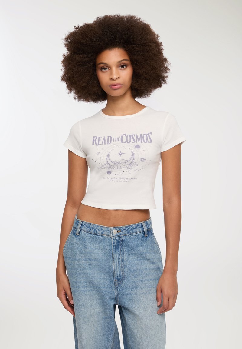 Biała krótka koszulka z grafiką "READ the COSMOS" w kolorze fioletowym. Połączona z jasnoniebieskimi, wysokim stanem dżinsami. Gładka faktura.