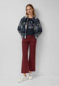 Geruite flanellen jas in marineblauw en beige, marineblauw graphic t-shirt, bordeaux flared broek en witte sneakers. Eenvoudig ontwerp met contrasterende kleuren.