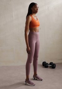 Treningstøy med en oransje sports-bh, lyserøde høytaljede tights med sidelomme, og lilla joggesko med teksturert såle.