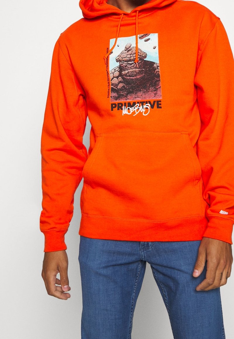 Sudadera naranja de algodón. Presenta un estampado gráfico con texto en la parte delantera, bolsillo tipo canguro y capucha con cordón ajustable.