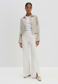 Beige linnen cropped jack met knopen aan de voorkant en twee zakken, gecombineerd met hoge witte flare jeans met zijsplitten en beige flats.