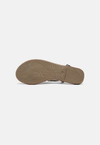 Shoe sole features a textured, wavy pattern in light brown rubber. The upper section shows a dark, muted color and simple design with minimal accents.