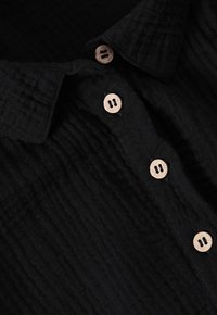 Camicia nera con colletto realizzata in un tessuto testurizzato, caratterizzata da cinque bottoni in legno sul davanti e un delicato design a piè di melo.
