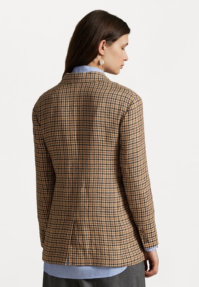 Gecheckt blazer in bruin en zwart met een getailleerde pasvorm, twee achterste splitten en knoopmanchetten, gedragen over een lichtblauw overhemd.