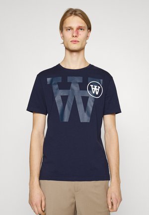 Tricou din bumbac de culoare bleu marin, cu un mare logo alb „W” uzat și un logo accent circular alb pe piept. Mâneci scurte și decolteu rotund.