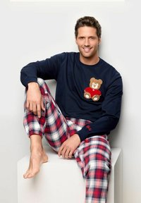 Parte superior de pijama de manga larga en azul marino con un diseño de oso de peluche, combinada con pantalones de franela a cuadros rojos y blancos con puños elásticos.