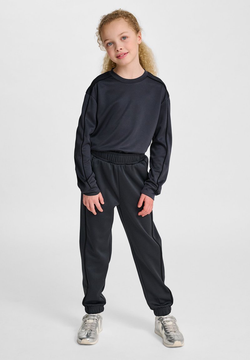 Svart långärmad träningsöverdel med rund halsringning, tillsammans med matchande svarta joggers med elastisk midja och avslutade anklar.