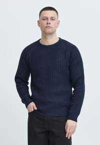 Navy ribbed knit sweater with crew neck and long sleeves. Made from textured fabric, featuring subtle variations in shade.