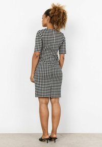 Mustat ja valkoiset houndstooth-kuosiset, vartalonmyötäiset mekko, jossa on lyhyet hihat, takana halkio ja polvenmittainen helma. Yhdistetty mustiin korkokenkiin.