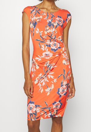 Femme portant une robe orange sans manches, longueur genoux, avec des motifs floraux roses et bleus et un tissu froncé à la taille.