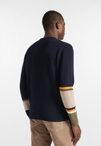 Maglione navy a maglia con scollatura rotonda e maniche a righe multicolore in beige, marrone, arancione e verde. Finitura texturizzata con orlo a coste.