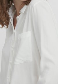 Chemise blanche boutonnée en tissu léger, dotée d'une poche poitrine, d'un col standard et d'une texture douce avec une coupe décontractée.
