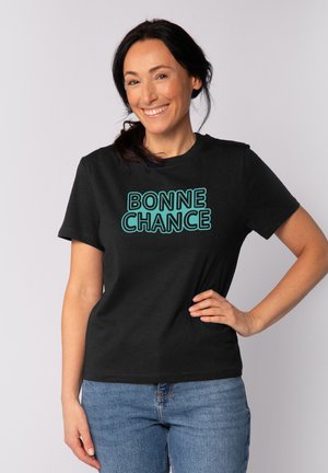 Zwarte T-shirt met korte mouwen met "BONNE CHANCE" in turquoise tekst. Casual ontwerp met een gladde textuur, gecombineerd met blauwe spijkerbroek.