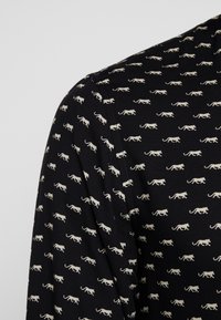 Top de tela negra con un patrón repetido de pequeños leopardos blancos. La textura parece suave y el diseño incluye un escote redondo.