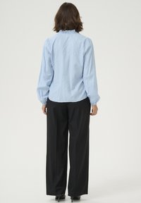 Light blue, textured blouse with a high collar and puffed sleeves, paired with black, wide-leg trousers and black heels.