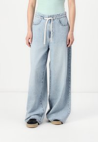 Jean large bleu clair en denim, doté d'une taille à cordon de serrage, de poches avant et d'une texture légèrement délavée.