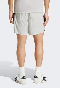 Helle graue Shorts aus einem strukturierten Stoff, mit seitlichen Taschen und einer Gesäßtasche, getragen mit weißen Socken und schwarz gestreiften Schuhen.