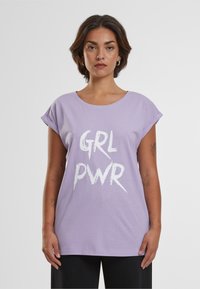 Lavendel bomulds t-shirt med rullede ærmer og en afslappet pasform. Har fed hvid tekst "GRL PWR" i en graffiti-lignende skrifttype på forsiden.