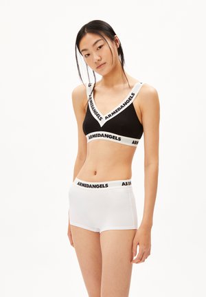 Zwarte bralette met witte, gebrandmerkte banden, gecombineerd met witte boxershorts met een bijpassende tailleband, wat de tegenstelling in kleuren en materialen benadrukt.