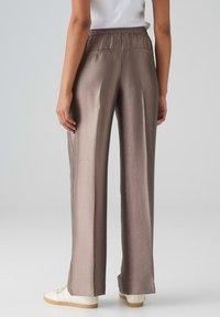 Lichtbruine, brede broek gemaakt van een gladde, licht glanzende stof. Heeft een elastische tailleband en minimalistische achterzakken.