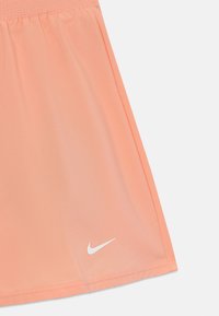 Persikofärgad sportkjol i lätt material, med ett elastiskt midjeband och en vit Nike-logga vid fåll.