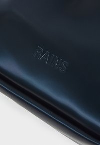 Navyblaues, wasserdichtes Material mit glatter Textur. Verfügt über das eingeprägte "RAINS"-Logo. Schlichte, rechteckige Form mit klaren Linien.