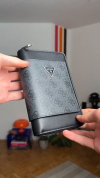 Must rahakott, millel on tekstuuriga disain ja Guessi logo. Sellel on tõmblukuga sulgemine, nahast detailid ja sile viimistlus.