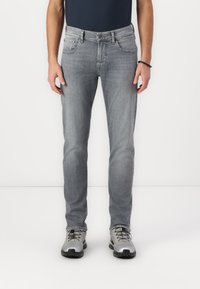 Grå denim jeans med rett passform, fem lommer og knappest fly. Bært med grå utendørssko, kombinert med en marineblå skjorte.