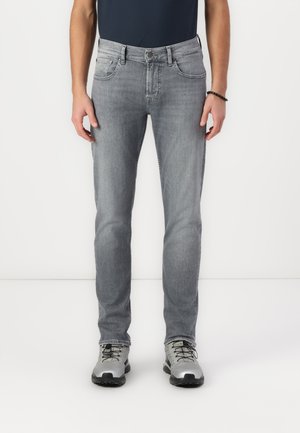 Jeans en denim gris avec une coupe droite, cinq poches et une fermeture à bouton. Portés avec des chaussures de plein air grises, associés à une chemise navy.