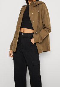 Brun huvad jacka i ett lättviktigt tyg, med dragkedja fram, tryckknappar och sidofickor, tillsammans med svarta cargobyxor.