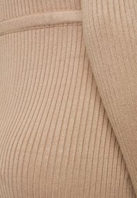 Gros plan d’un tissu en maille côtelée beige montrant des lignes verticales et une texture avec une zone pliée sur le côté droit.