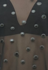 Čierny priehľadný top s hlbokým výstrihom do V a textúrovanou látkou zdobenou kruhovými, kovovými striebornými akcentmi po celej ploche.