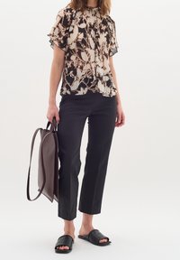 Zwart-beige geplooide blouse met bloemenpatroon, korte mouwen; gecombineerd met zwarte slanke broek en zwarte slippers. Inclusief bruine shopper tas.