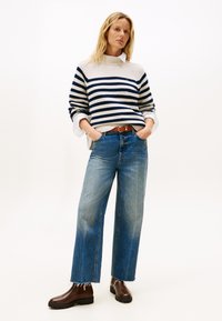 Gestreifter Strickpullover in Creme und Navy, weite blaue Jeans und braune Knöchelstiefel. Der Pullover hat gerippte Bündchen und ein strukturiertes Schulterdesign.