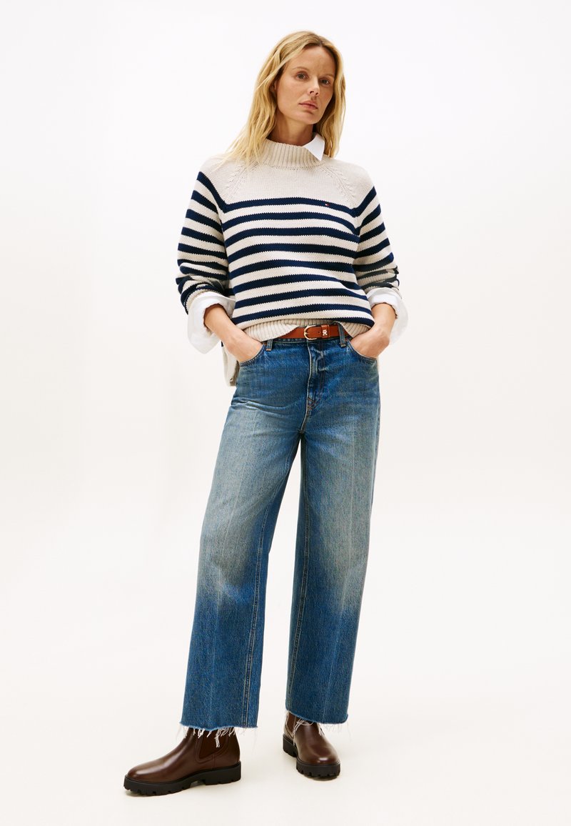 Gestreifter Strickpullover in Creme und Navy, weite blaue Jeans und braune Knöchelstiefel. Der Pullover hat gerippte Bündchen und ein strukturiertes Schulterdesign.