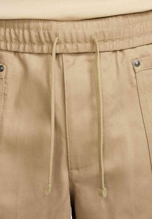 Pantaloni beige con coulisse realizzati in tessuto testurizzato, dotati di una vita elastica e due aperture per tasche con dettagli metallici.